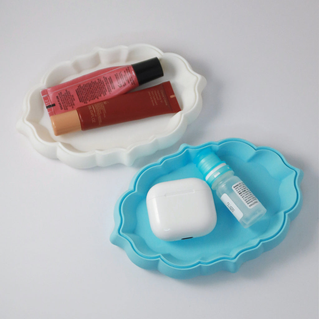 Two small cloud-shaped trays, one white and one blue, with cosmetic products on a light gray background.